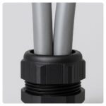 Close-up of a plastic cable gland with two grey 25mm² PVC meter tails entering a metal consumer unit.